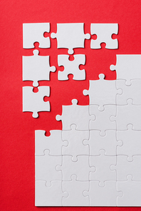 top view of white connected and separate jigsaw puzzle pieces isolated on red