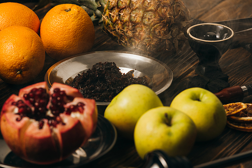 hookah, tobacco, apples, oranges, garnet and pineapple on wooden surface