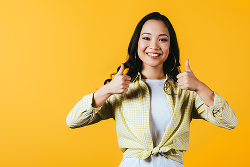 smiling asian woman showing thumbs up isolated on yellow