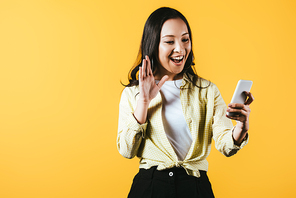 happy asian girl waving and making video call on smartphone isolated on yellow
