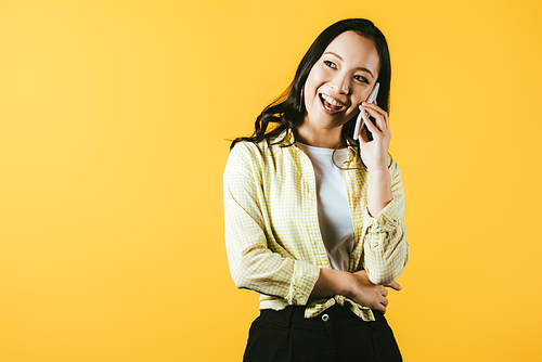 brunette asian girl talking on smartphone isolated on yellow