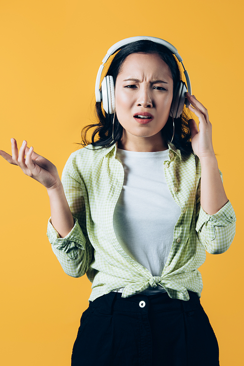 confused asian girl listening music with headphones, isolated on yellow