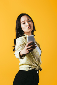beautiful asian girl taking selfie on smartphone isolated on yellow
