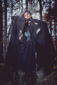 low angle view of woman in witch costume and crown on head holding hands with black textile near face