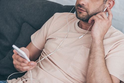 cropped view of adult man holding smartphone and listening music in earphones