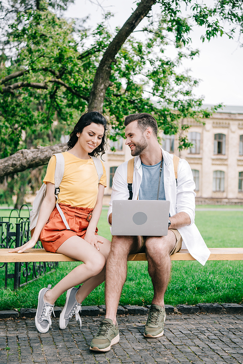 young woman sitting on bench near man using laptop