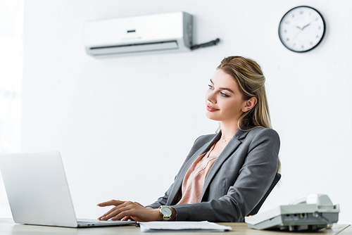 happy businesswoman sitting in office with air conditioner and usinglaptop