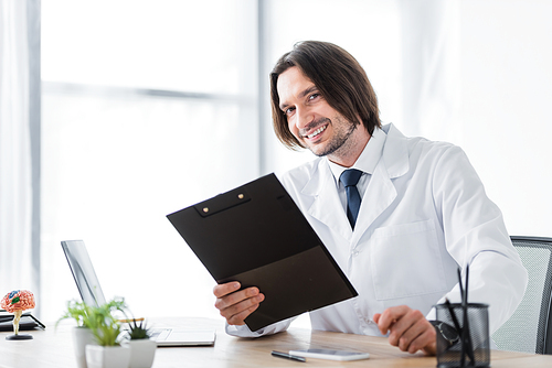 happy doctor with clipboard in hand  while sitting in office