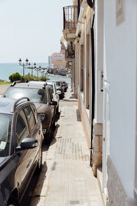 Urban street with row of cars, buildings and sea with blue sky at background in Catalonia, Spain