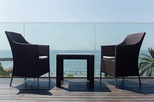Low angle view of table and chairs near glass fencing and seascape at background in Catalonia, Spain