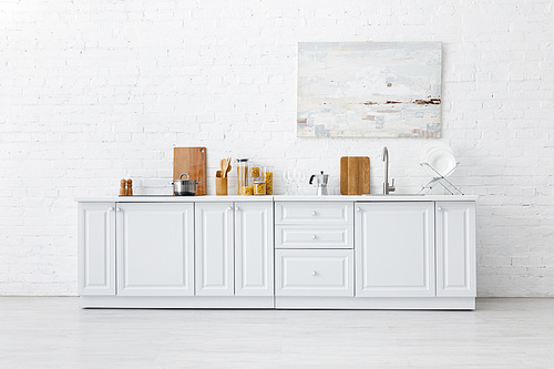 minimalistic white kitchen interior with kitchenware and painting on brick wall