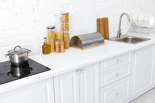 minimalistic modern white kitchen interior with kitchenware near brick wall