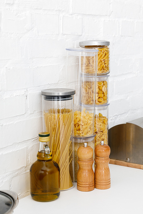 raw pasta in food containers, oil and bread box near white brick wall