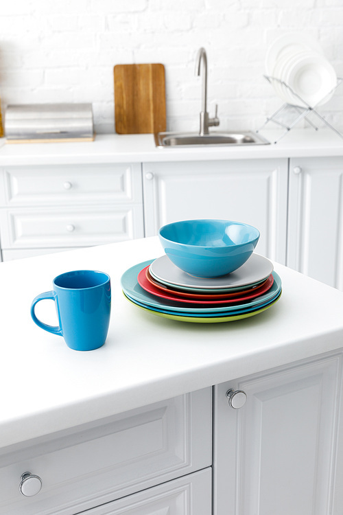 selective focus of colorful plates and cup with kitchenware near brick wall on background