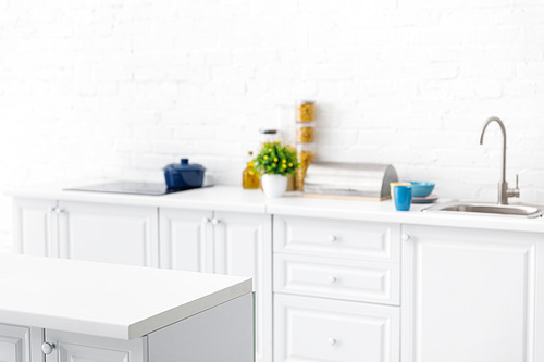 selective focus of modern white kitchen interior with kitchenware near brick wall