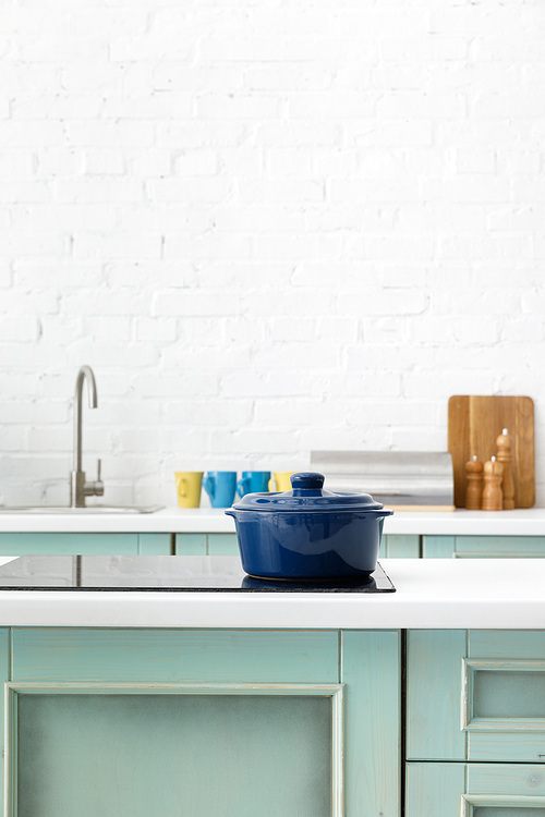 selective focus of white and turquoise kitchen interior with pot on electric induction cooktop