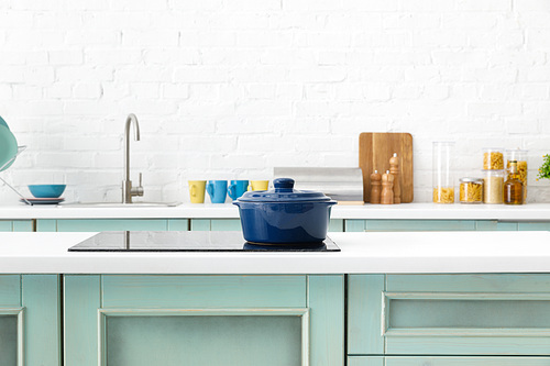 selective focus of modern white and turquoise kitchen interior with pot on electric induction cooktop