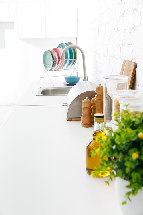 selective focus modern white kitchen interior with kitchenware and green plant near brick wall