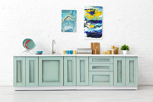 modern white and turquoise kitchen interior with kitchenware and abstract paintings on brick wall