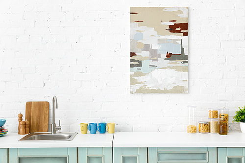 modern white and turquoise kitchen interior with kitchenware and abstract painting on brick wall