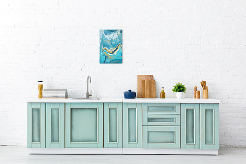 white and turquoise kitchen interior with kitchenware and abstract painting on brick wall