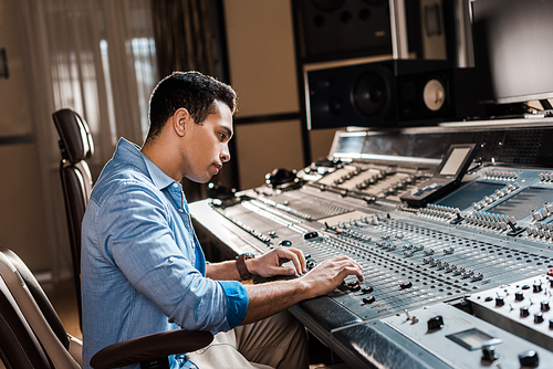 attentive mixed race sound producer working at mixing console in recording studio
