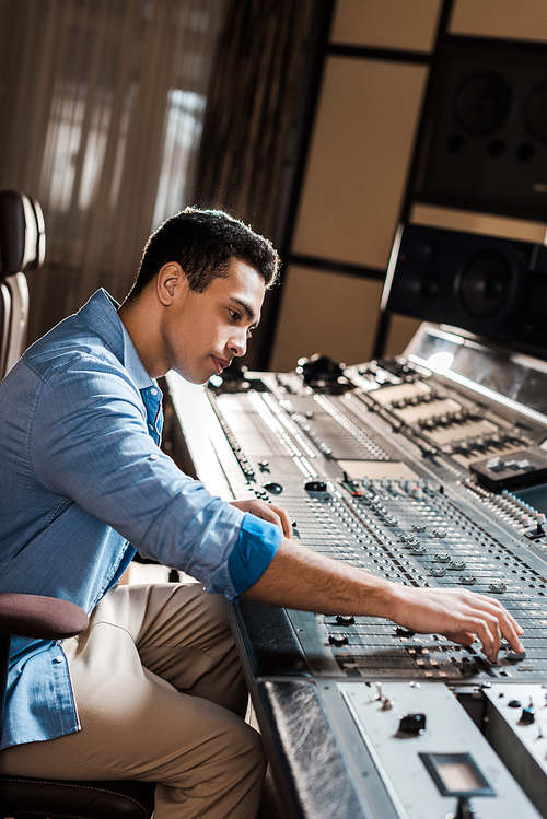 handsome mixed race sound producer working at mixing console in recording studio