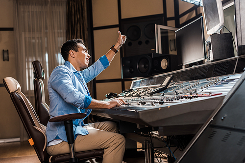 smiling mixed race sound producer showing thumb up while working at mixing console
