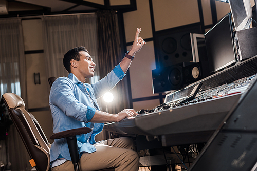 handsome mixed race sound producer showing victory sign while working in recording studio