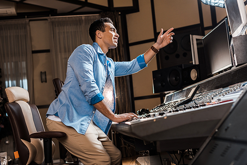 handsome mixed race musician gesturing while working at mixing console