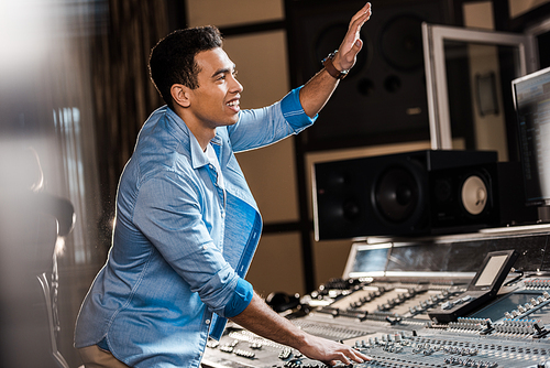 selective focus of smiling mixed race sound producer gesturing while working in recording studio