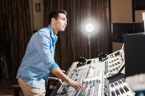 attentive mixed race sound producer working at mixing console in recording studio