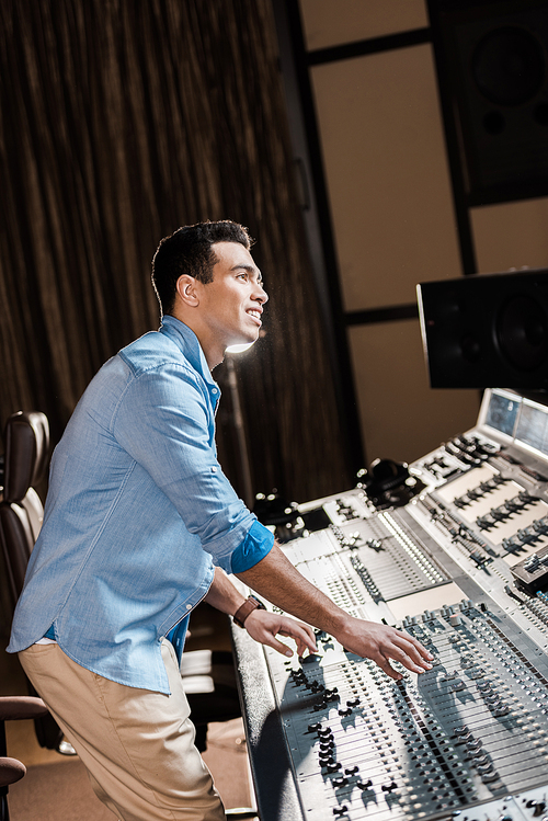 smiling mixed race musician working at mixing console in recording studio