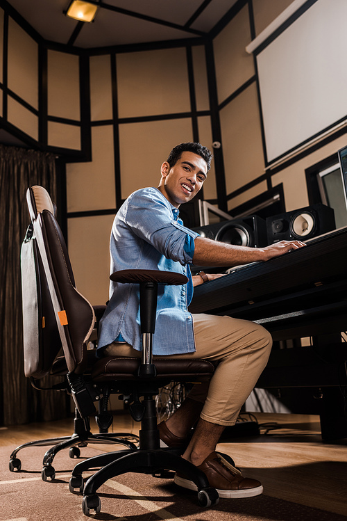 smiling mixed race sound producer sitting in office chair in recording studio and 