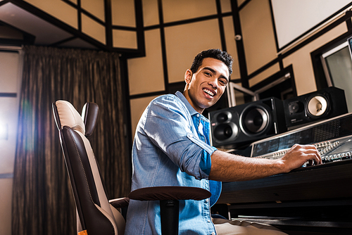 cheerful mixed race sound producer sitting in office chair in recording studio and 