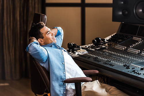 handsome smiling mixed race sound producer resting in office chair in recording studio