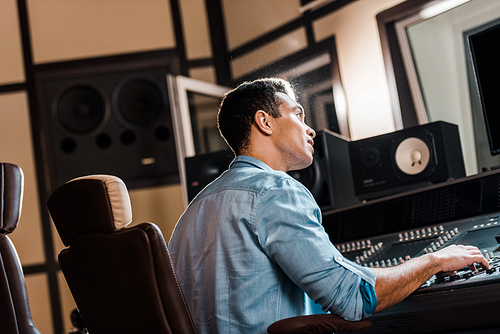 attentive mixed race sound producer working at mixing console in recording studio