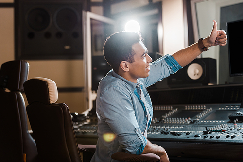 smiling mixed race sound producer showing thumb up while working in recording studio