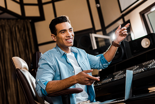 handsome cheerful mixed race sound producer gesturing while working in recording studio