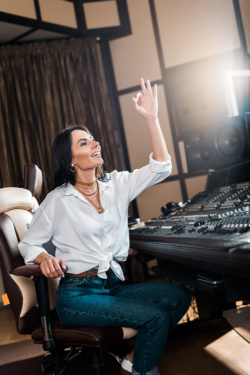 attractive sound producer showing ok sign and smiling in recording studio