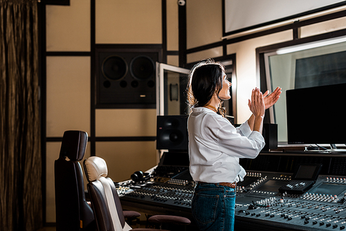 attractive sound producer applauding in recording studio near mixing console