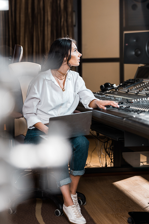 selective focus of attractive sound producer with laptop working at mixing console