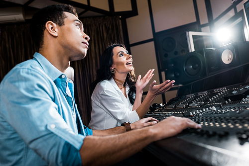 selective focus of attractive sound producer gesturing near handsome mixed raced colleague working at mixing console