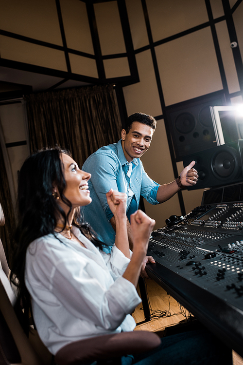 two happy multicultural sound producers showing success gestures in recording studio