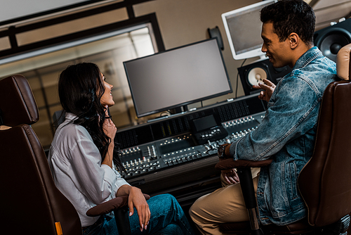 two young smiling sound producers working sitting near mixing console while working in recording studio