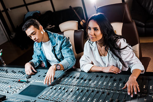 two young attentive multicultural sound producers working at mixing console in recording studio