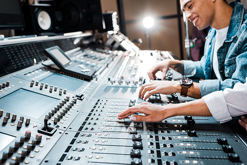cropped view of woman working at mixing console with mixed race colleague in recording studio
