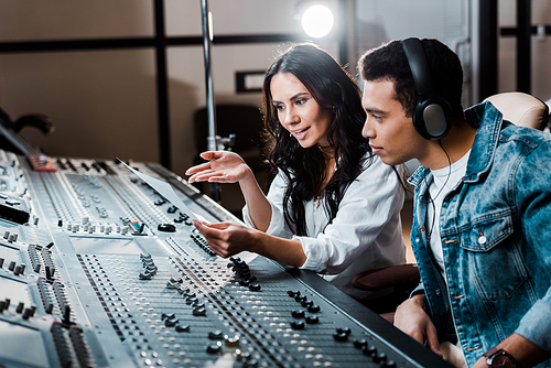 two young multicultural sound producers working at mixing console in recording studio