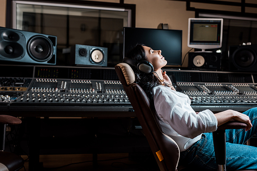 pretty sound producer listening music in headphones while sitting in office chair in recording studio
