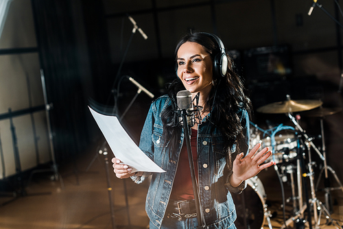 selective focus of smiling woman singing in recording studio near microphone